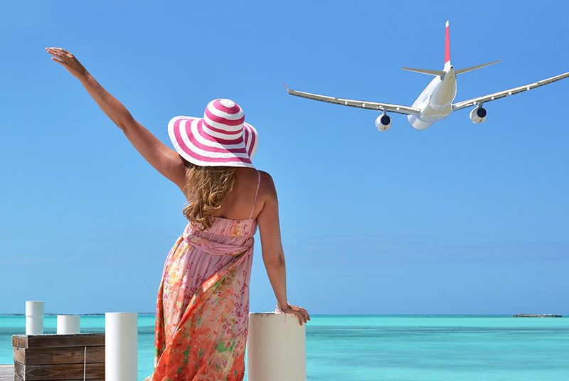 A woman waves off a plane on a beach|A man and woman stand underneath a tree|Q woman with blue rubber gloves cleans a sideboard|Folded towels and cleaning products