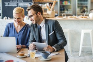 Two people sitting in a cafe looking at laptop and tablet