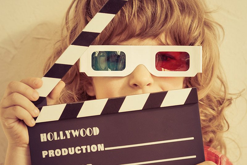 A girl wearing 3D glasses and holding a clapperboard which says Hollywood on it.