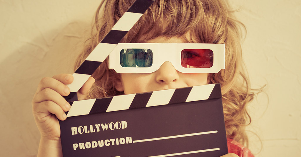 A girl wearing 3D glasses and holding a clapperboard which says Hollywood on it. 