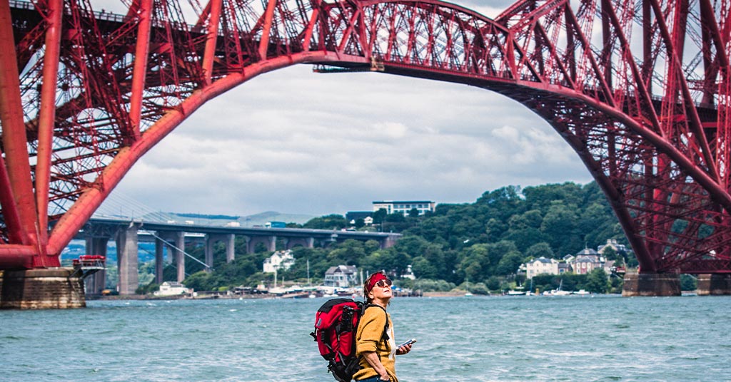 A tourist looking in awe around the red Forth Railway Bridge. 