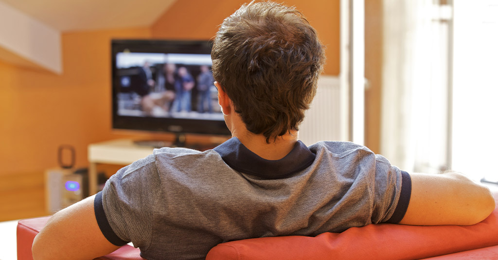 A man is relaxing in a chair watching TV. 