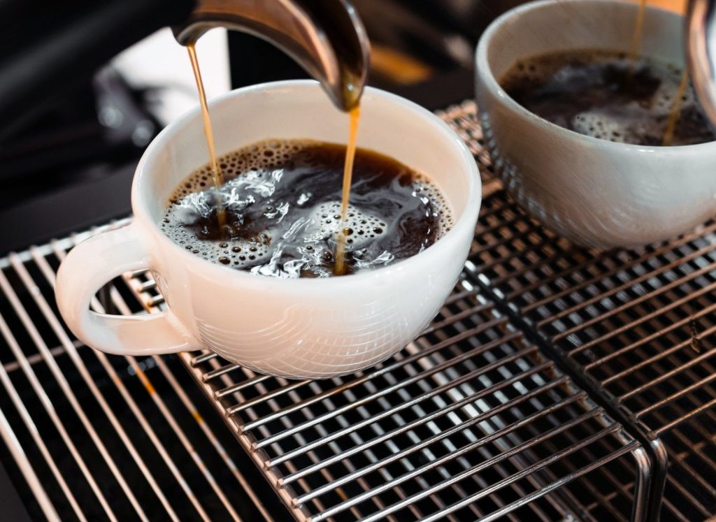 White cup of black coffee being brewed from an espresso machine.