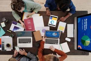 Digital marketing image of people with laptops, tablets, and reports on a table